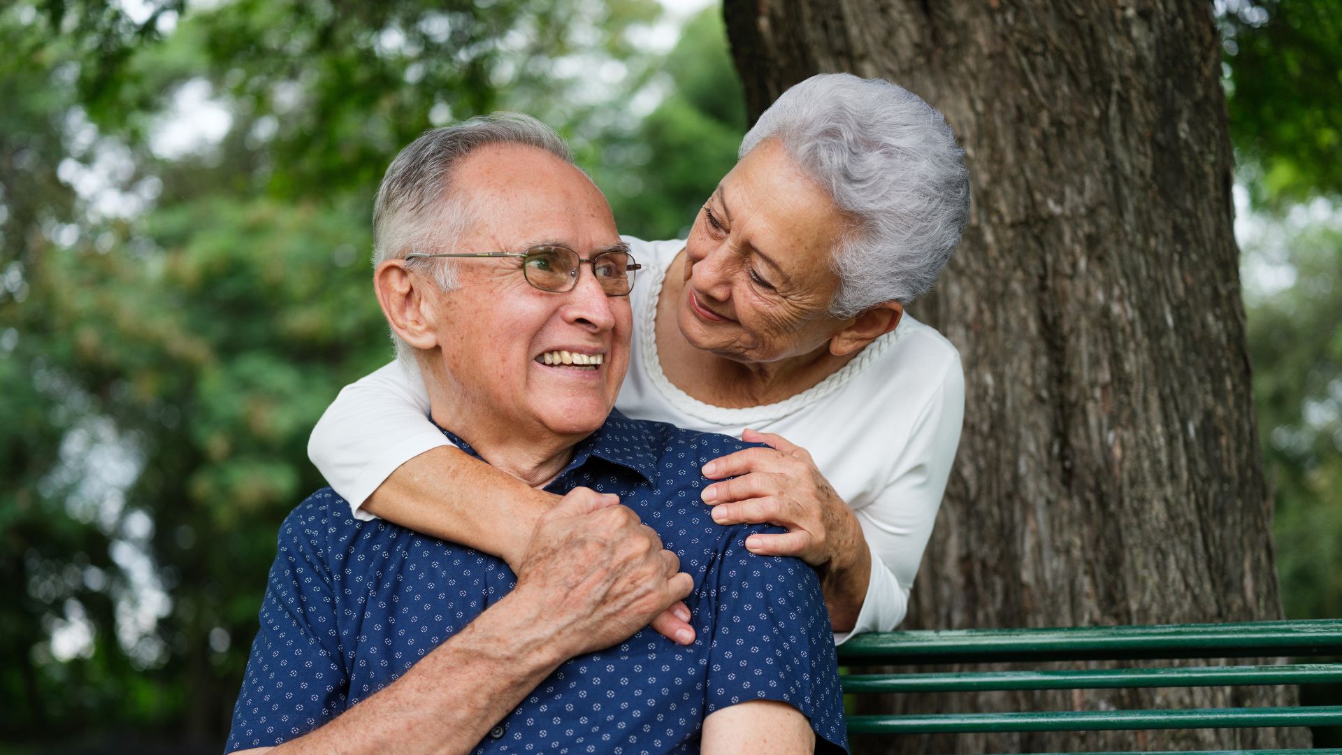 Casal idoso sorridente por ter feito planejamento previdenciário sentado em um banco de parque.